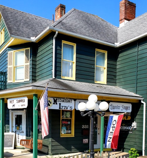 A green building with yellow trim, featuring a pet supply store and "Midnight Izzy's" sign, with an open flag and American flag.