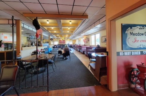 Interior of a diner with booths and tables, featuring a cozy atmosphere and a view of the kitchen area.