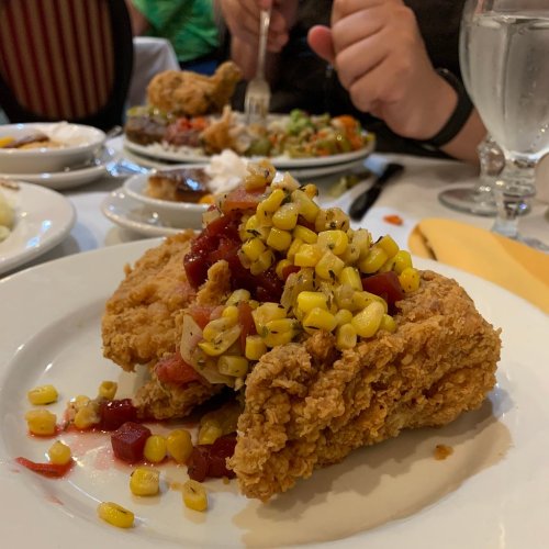 A plate of fried chicken topped with corn salsa, surrounded by side dishes on a dining table.