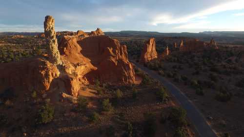 A scenic view of red rock formations and a winding road under a blue sky with scattered clouds.