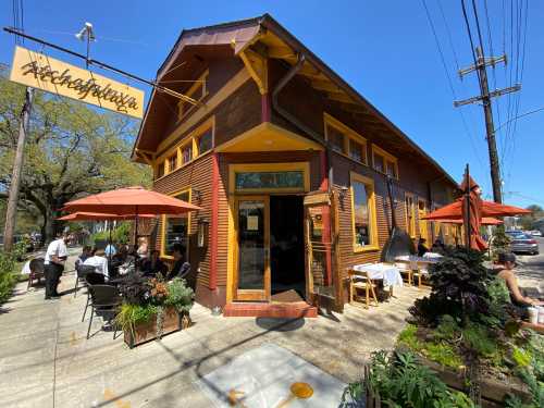 A charming restaurant with a wooden exterior, outdoor seating, and umbrellas on a sunny day.