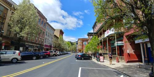 A vibrant street scene with historic buildings, trees, and blue skies, showcasing a lively urban atmosphere.
