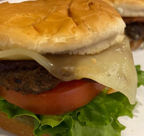 Close-up of a burger with a beef patty, melted cheese, lettuce, and tomato on a toasted bun.