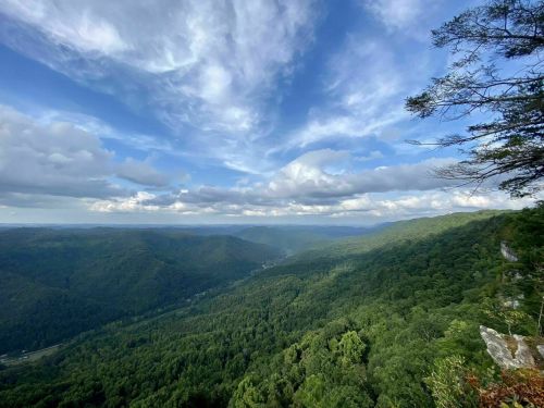 A panoramic view of lush green mountains under a cloudy sky, with valleys stretching into the distance.