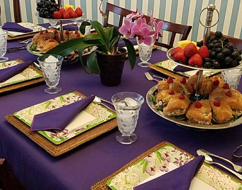 A beautifully set table with purple tablecloth, featuring fruit, pastries, and elegant glassware.