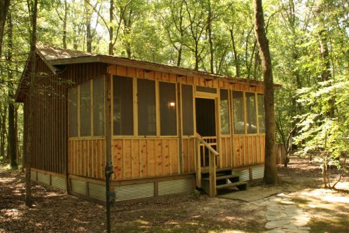 A wooden cabin with a screened porch, surrounded by trees in a forested area.