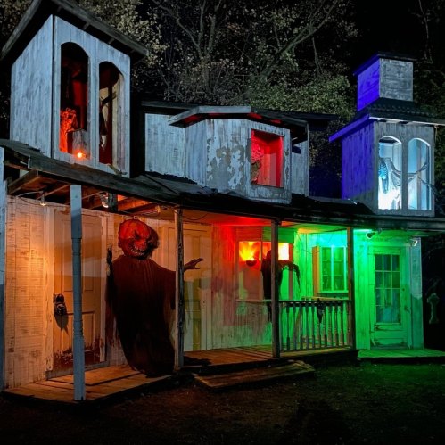 A spooky, dimly lit haunted house with eerie decorations and colorful lights at night.