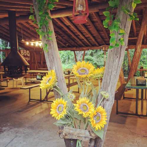 A rustic outdoor space with wooden beams, a lantern, and a bouquet of sunflowers in a planter.