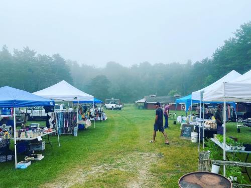 A misty outdoor market with blue tents, vendors, and shoppers walking along a grassy path.