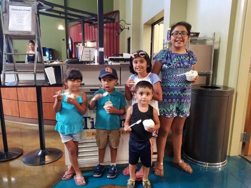 A group of five children enjoying ice cream at a shop, smiling and holding their treats.