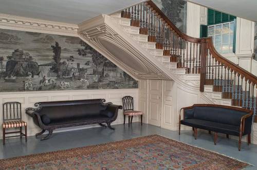 Elegant foyer with a grand staircase, vintage furniture, and detailed wall murals, featuring a patterned rug on the floor.