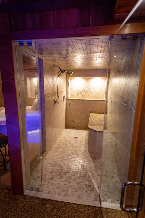 A modern, tiled shower with glass doors, featuring multiple showerheads and soft lighting.