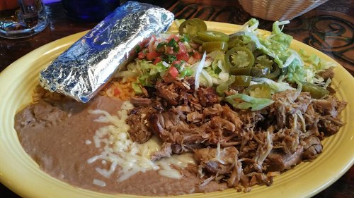 A colorful plate featuring shredded meat, refried beans, rice, lettuce, jalapeños, and a foil-wrapped burrito.