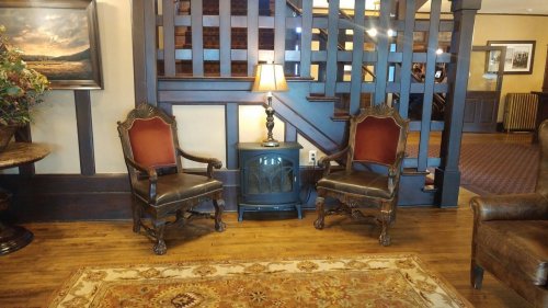 Two ornate chairs with red upholstery flanking a small table and lamp, set in a cozy, warmly lit interior.