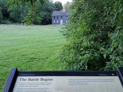 A historical sign about the Battle of Bunker Hill, with a grassy field and a house in the background.