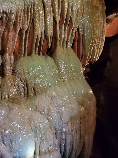 Close-up of a textured cave wall with greenish stalactites and stalagmites, showcasing natural mineral formations.