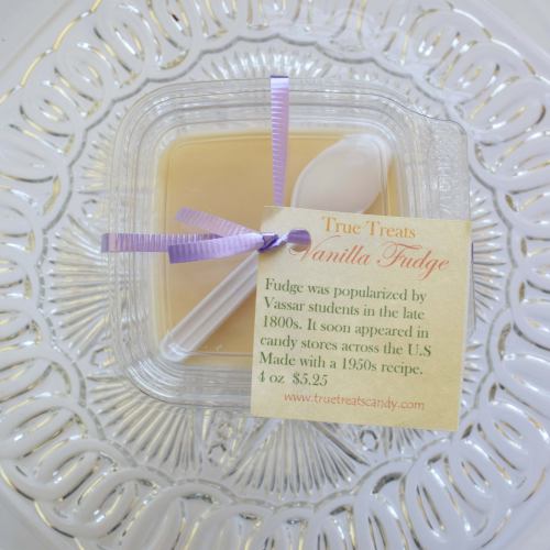 A clear container of vanilla fudge with a spoon, labeled "True Treats Vanilla Fudge," on a decorative plate.