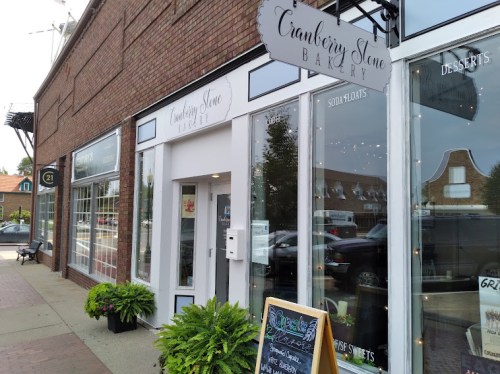 Exterior of Cranberry Stone Bakery, featuring a welcoming entrance, potted plants, and a chalkboard menu outside.