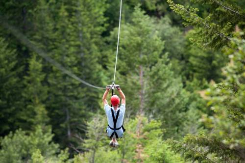 A person in a red helmet zip-lining through a forested area, surrounded by green trees.