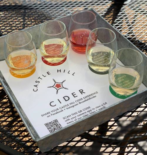 A tray with five tasting glasses of different ciders, featuring a QR code and branding for Castle Hill Cider.