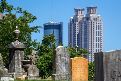 A cemetery with gravestones in the foreground and modern skyscrapers in the background under a clear blue sky.