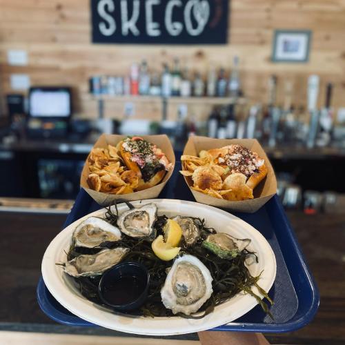 A tray with oysters on a plate and two boxes of nachos, set against a rustic bar backdrop.