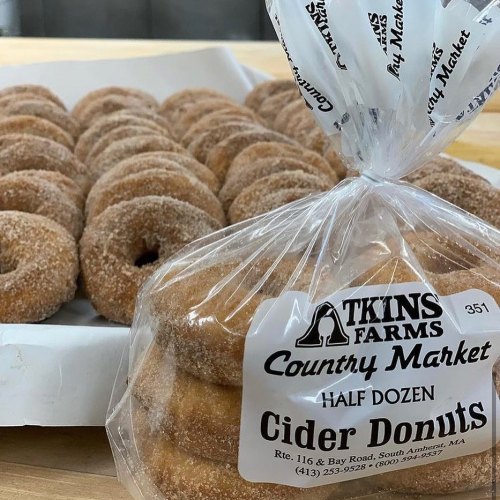 A bag of cider donuts from Atkins Farms Country Market, with a tray of more donuts in the background.