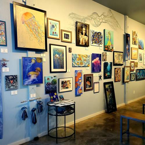Art gallery wall featuring various framed artworks, including jellyfish and abstract pieces, with a small table in front.