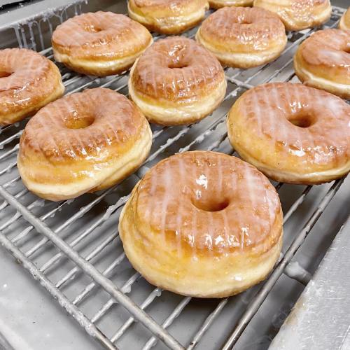 A tray of freshly glazed donuts, golden brown and shiny, arranged neatly in a bakery setting.