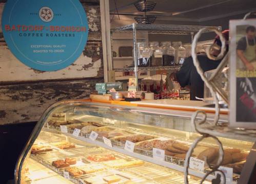 A coffee shop display case filled with pastries, with a barista working in the background and a sign for the roastery.