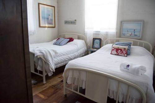 A cozy bedroom with two twin beds, light walls, and framed beach-themed artwork. Natural light filters through a window.