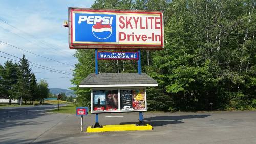 Sign for Skylite Drive-In featuring Pepsi logo, with movie posters displayed below, surrounded by trees.