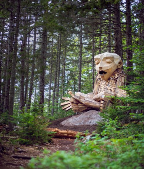 A large wooden sculpture of a seated figure surrounded by trees in a forest setting.