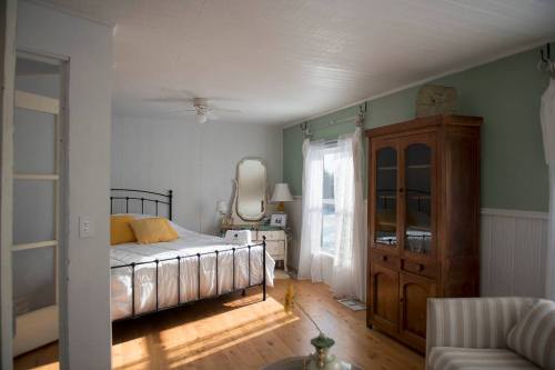 Cozy bedroom with a bed, wooden furniture, a mirror, and sunlight streaming through a window.