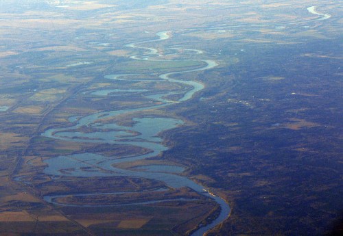Aerial view of a winding river surrounded by fields and greenery, showcasing a natural landscape.