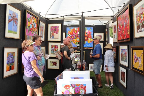A vibrant art booth at a fair, featuring colorful paintings and visitors admiring the artwork.
