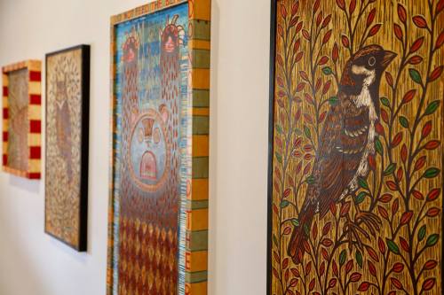 Four colorful framed artworks featuring intricate patterns and a bird, displayed on a white wall.