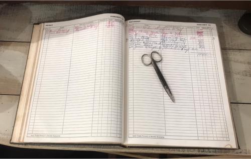 An open ledger book with handwritten entries and a pair of scissors resting on the pages.