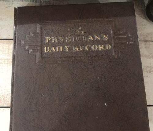 A brown leather-bound book titled "A Physician's Daily Record" resting on a wooden surface.