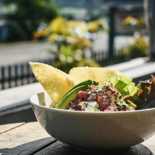 A bowl of fresh ceviche with tortilla chips and greens, set against a sunny outdoor backdrop.