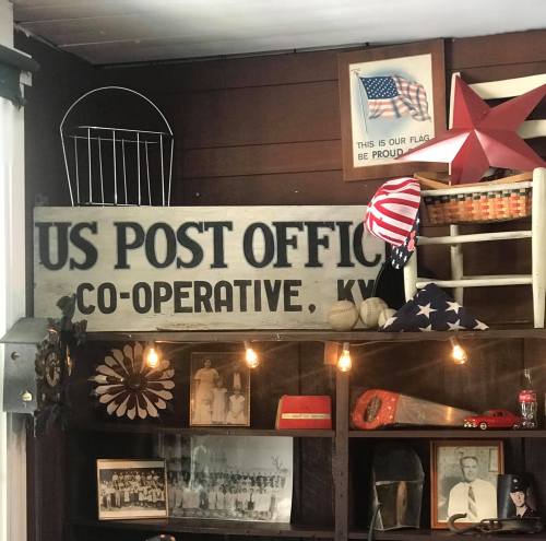 A vintage US Post Office sign with patriotic decor and historical photos displayed on a wooden wall.