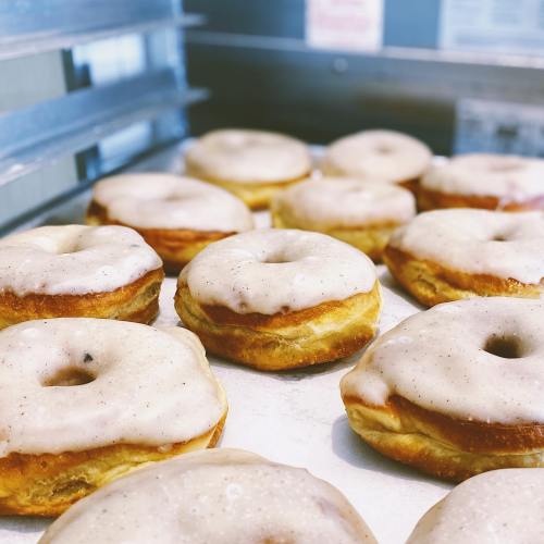 A tray of freshly baked donuts with a light glaze, arranged neatly in a bakery setting.
