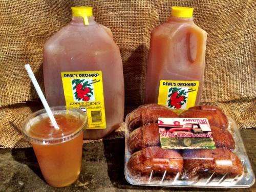 Two jugs of apple cider, a cup of cider with a straw, and a tray of donuts on a rustic background.