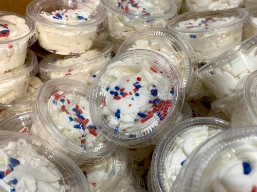 A close-up of plastic cups filled with whipped cream and red, white, and blue sprinkles.