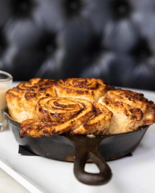 Freshly baked cinnamon rolls in a cast iron skillet, golden brown and gooey, served with a side of icing.