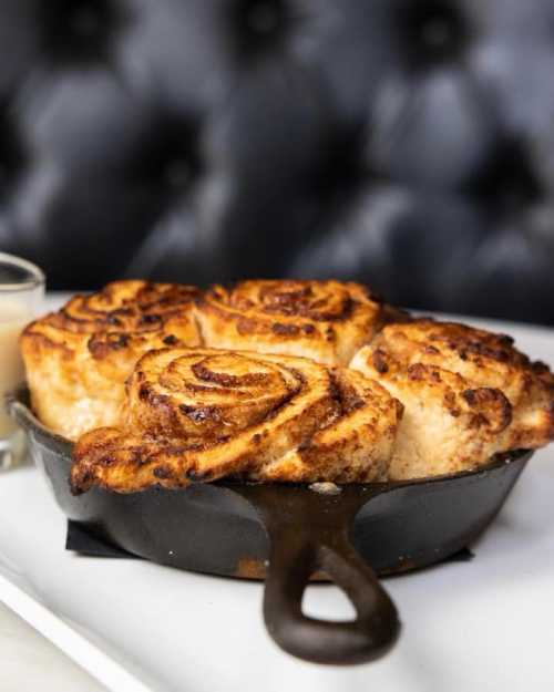 Freshly baked cinnamon rolls in a cast iron skillet, golden brown and gooey, served with a side of icing.