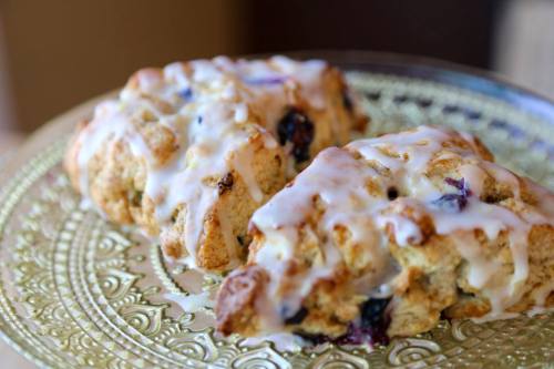 Two glazed blueberry scones on a decorative plate, showcasing a golden-brown texture and drizzled icing.