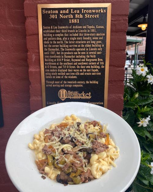 A plate of pasta with sausage and vegetables in front of a historical plaque about Seaton and Lea Ironworks.