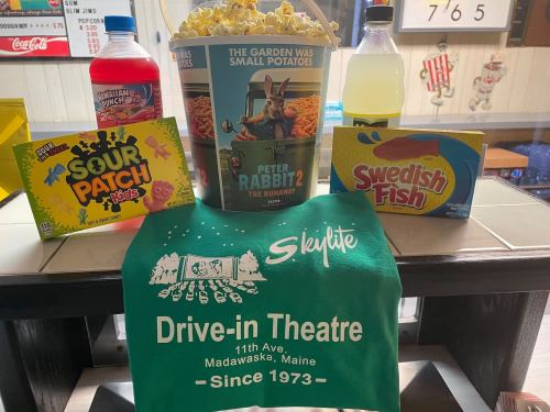 A drive-in theater setup featuring popcorn, drinks, candy, and a green Skilite Drive-in Theatre shirt.