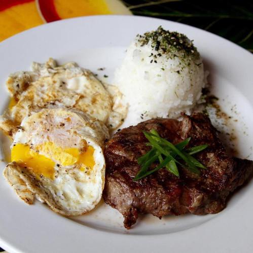 A plate featuring two fried eggs, a portion of rice, and a grilled steak garnished with green onions.